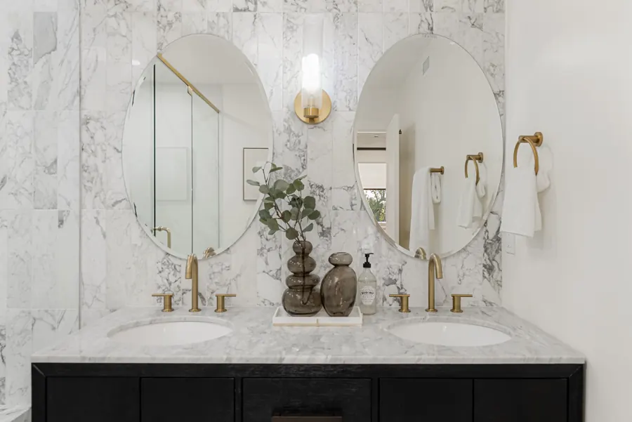 Black double vanity with oval mirrors and marble tile