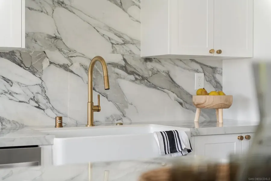 Brass faucet and farmhouse sink against marble backsplash