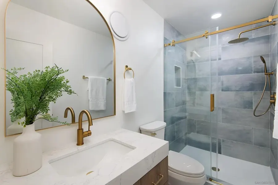 Bathroom with arched brass mirror and blue-tiled shower
